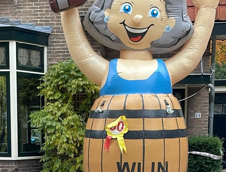 Opblaas pop Sarah met blauwe jurk in bruin wijnvat aan de voorkant van een huis