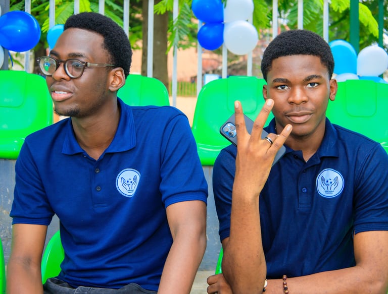 two men sitting on green chairs in front of a fence