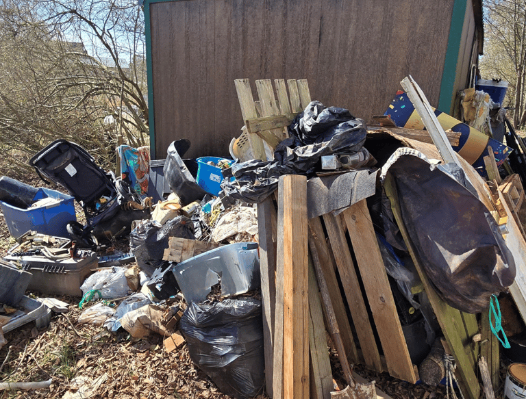 Storage building surrounded by trash, old stroller, old fencing, and more.