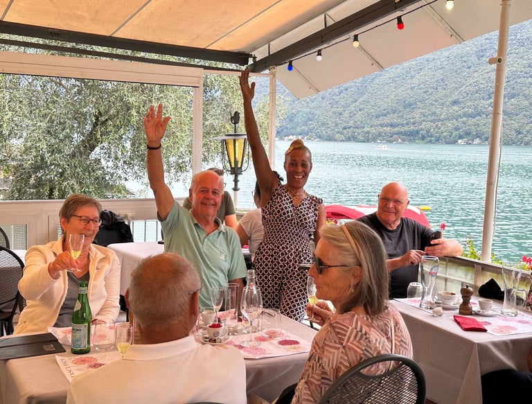 Un gruppo di persone sedute al tavolo su una terrazza con vista lago con bicchieri da vino