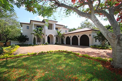 spanish style luxury home with an L shaped driveway and trees and red flowers and autumn leaves