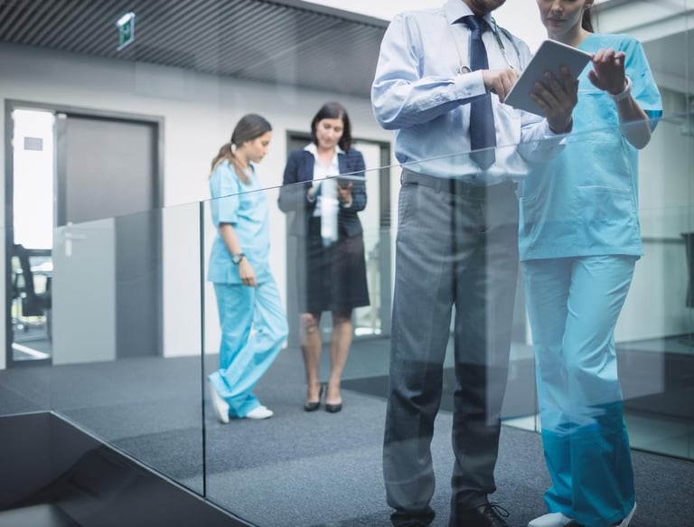 Equipo médico profesional es asesorado por ejecutivos de negocios revisando datos en una tableta