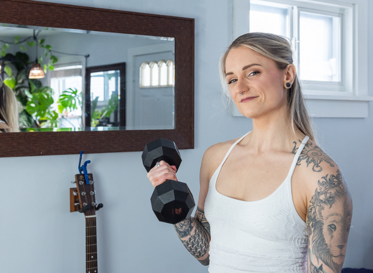 Jess Bartlett smiling warmly into the camera standing in a living room with a dumbbell
