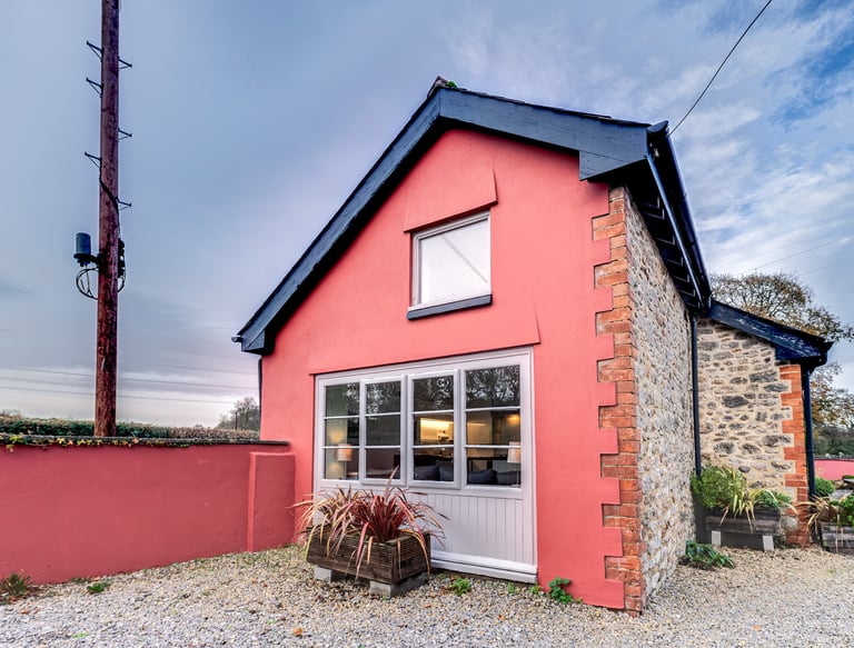 A charming pink cottage with stone walls and large windows, perfect for a cozy vacation rental.