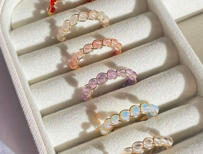 Anillos de cristal envueltos en alambre con cuentas de colores en una caja organizadora blanca.