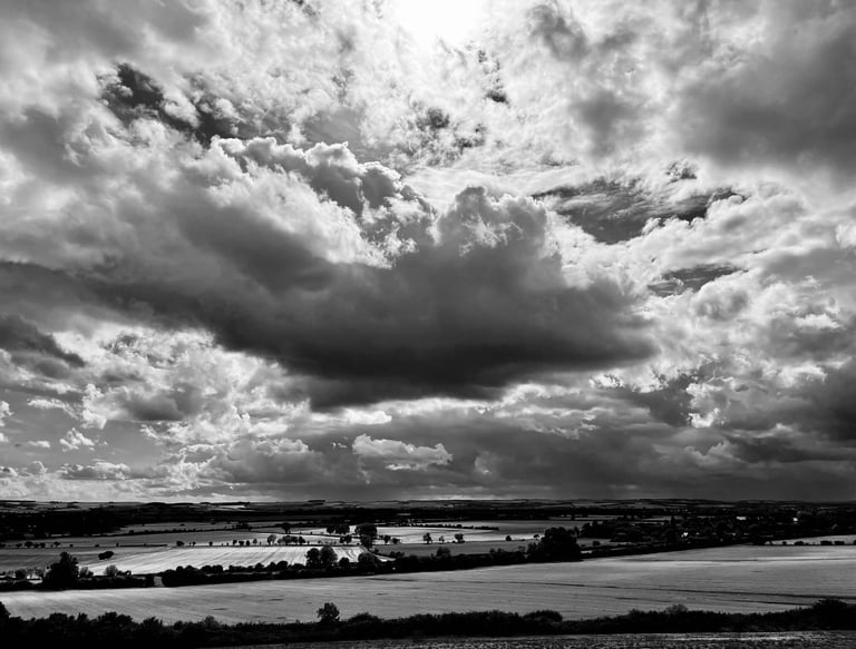 Black and white landscape of dramatic storm clouds over rolling rural farmland fields.