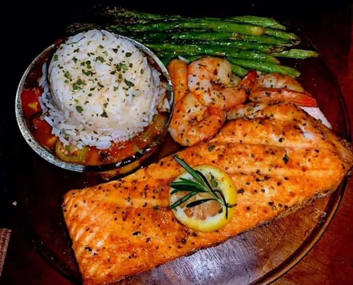 Grilled salmon fillet served with garlic shrimp, white rice, and roasted green asparagus on a plate.