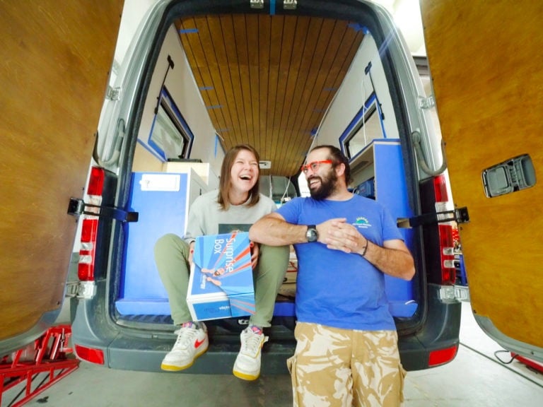a man and woman standing in a van with surfboards