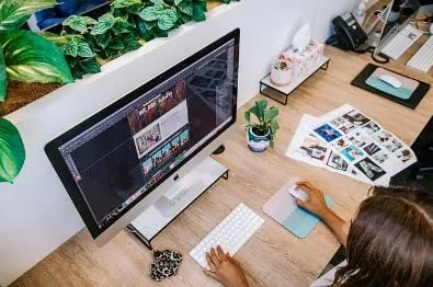 Chica diseñando una web en una mesa de oficina con flores y archivos en la mesa