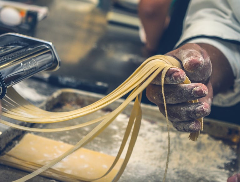 Close-up of a person’s hands making fresh tagliatelle with a pasta machine