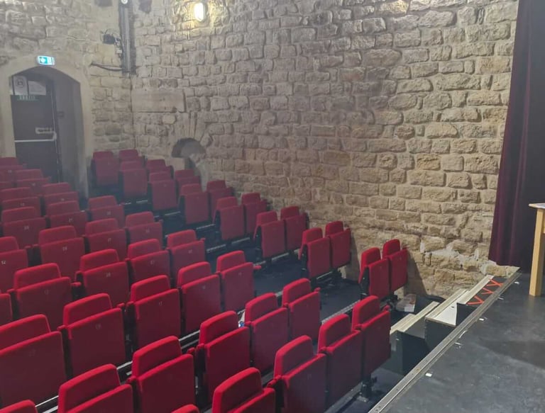 Intérieur d’un petit théâtre à l’ambiance intimiste, avec des rangées de fauteuils rouges face à une