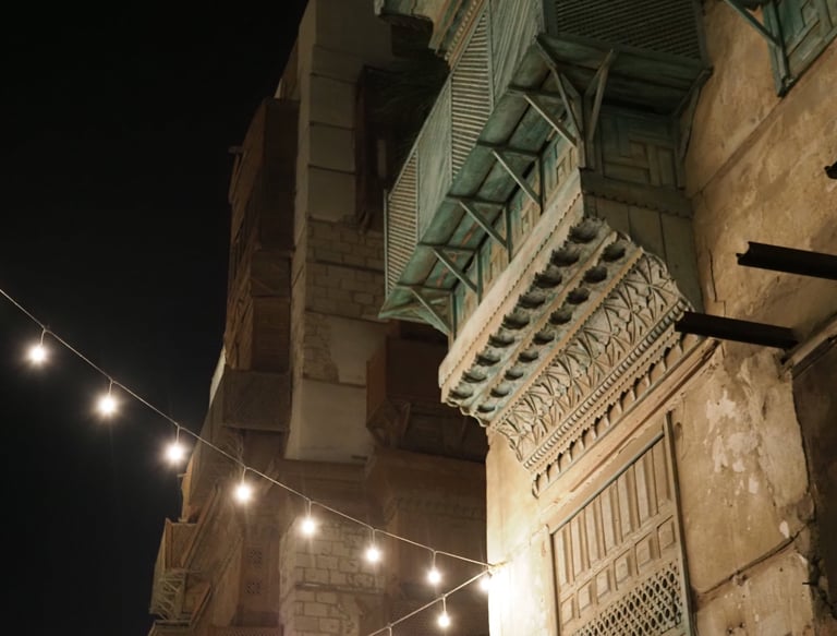 the facad of an old building in Jedda, the Tiffany blue mashrabia can be seen with lights at night