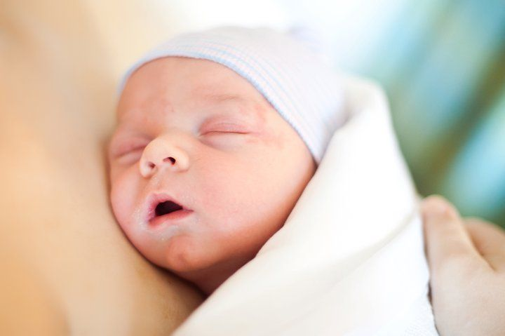 A peaceful newborn baby sleeping in a hospital swaddle blanket and blue striped beanie.