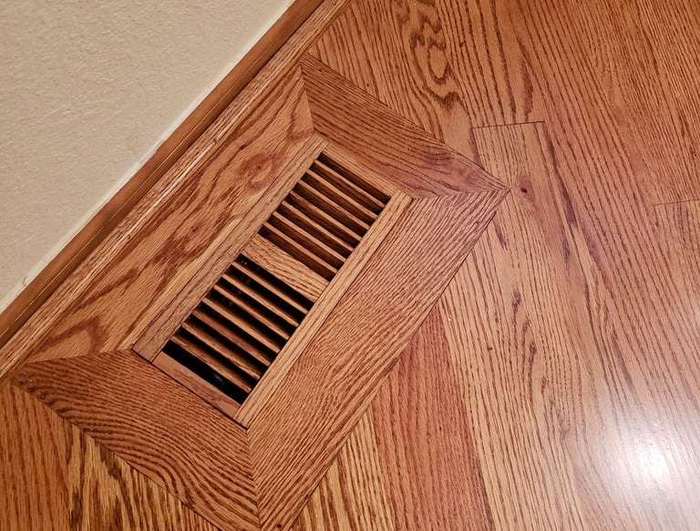 A flush mount wood floor vent cover integrated into a polished oak hardwood floor.