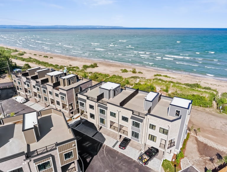 Aerial view of modern luxury beachfront townhomes with rooftop patios overlooking a sandy beach and blue waves.