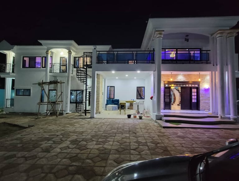 Luxury white two-story modern house illuminated at night with a spiral staircase and stone driveway.