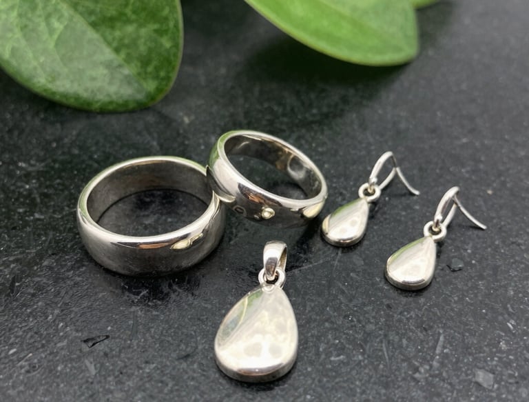Close-up of handcrafted silver jewelry pieces arranged on a soft jade green fabric.