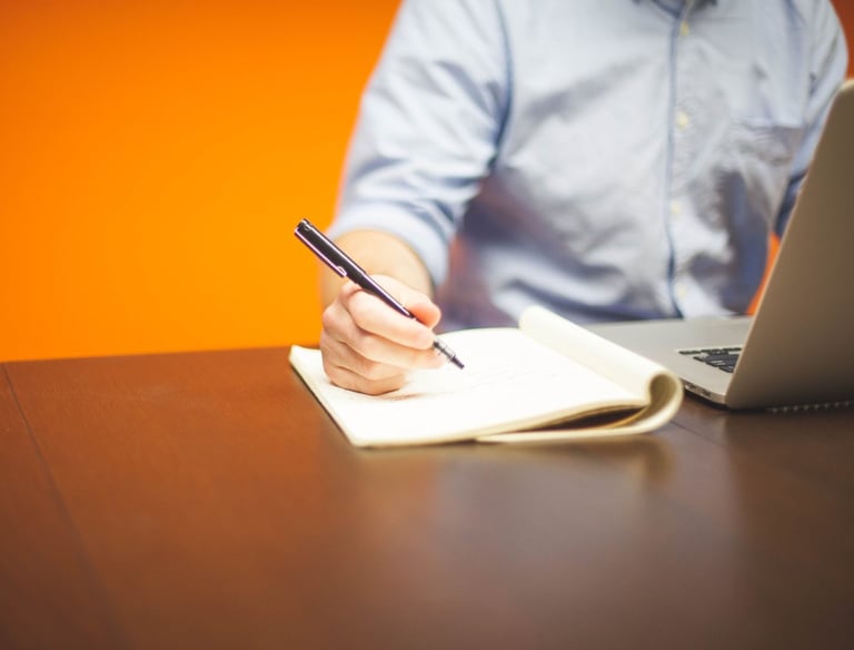 A person at a desk with laptop, pen and paper