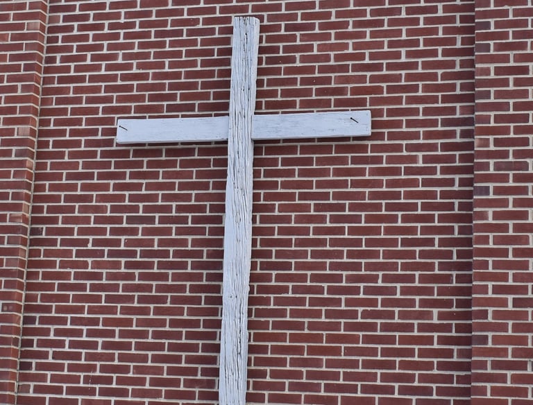 wooden cross hanging on a brick wall 