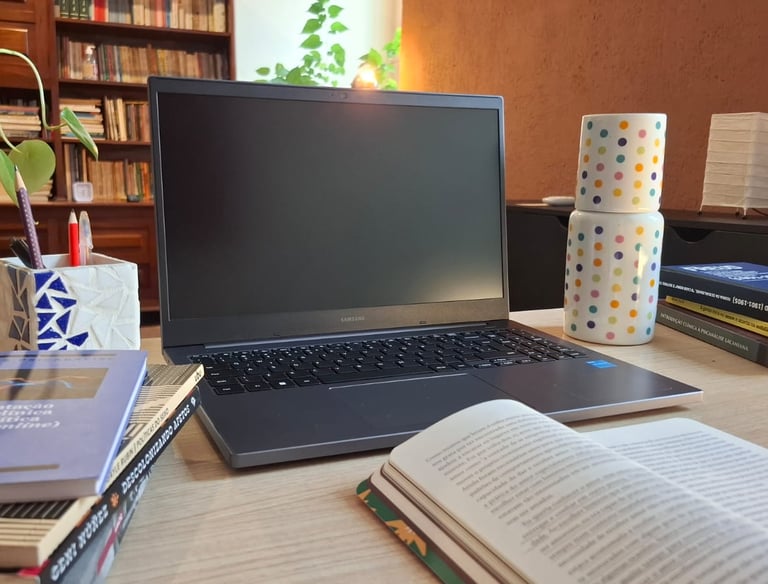 Mesa de trabalho com livros de autoras como Ana Suy, Gayle Rubin e Geni Núñez, ao lado do notebook u