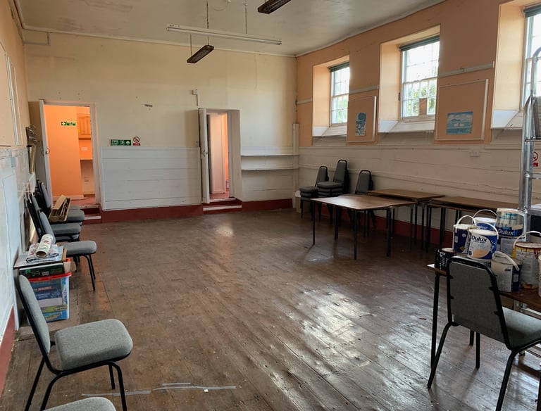 Former school hall with worn wooden floors and original windows before renovation