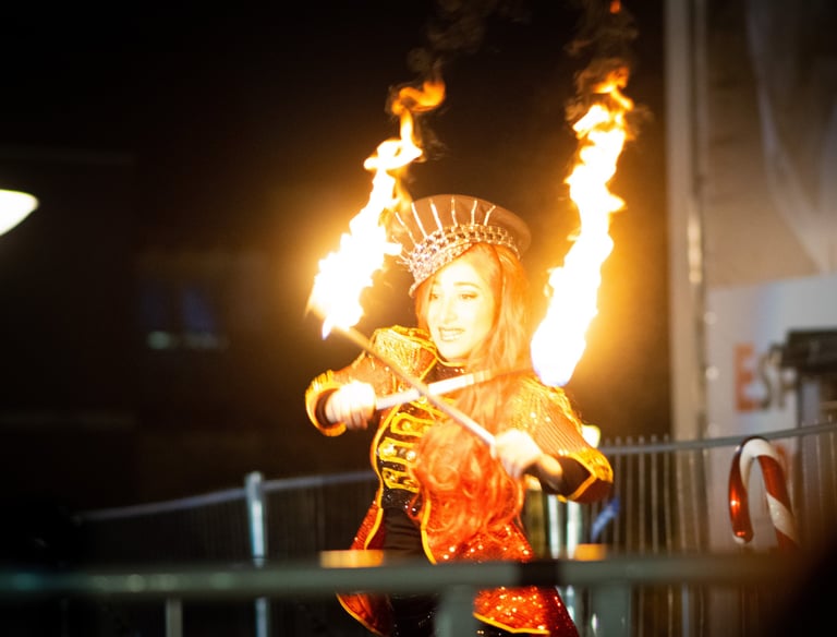 Une femme costumé en train de faire un spectacle avec des bâtons enflammés