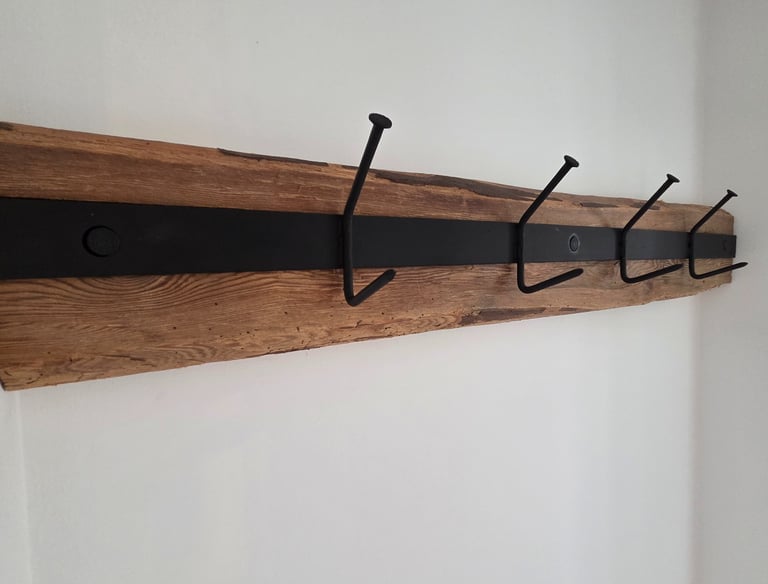 Wandgarderobe aus rustikalem Altholz mit schwarzem Metallband und vier massiven Eisenhaken im Industrial-Look.