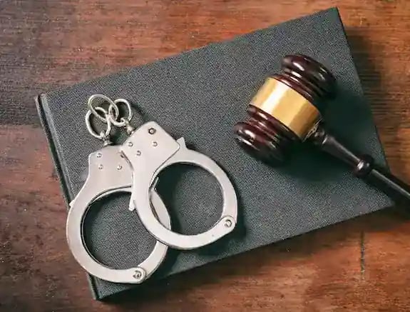 Esposas metálicas sobre un libro y mazo judicial, vista en primer plano.