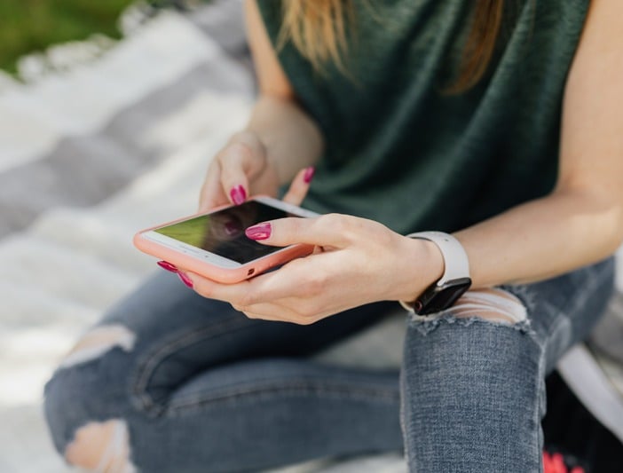 Photo of an adolescent girl with ripped jeans using a smartphone