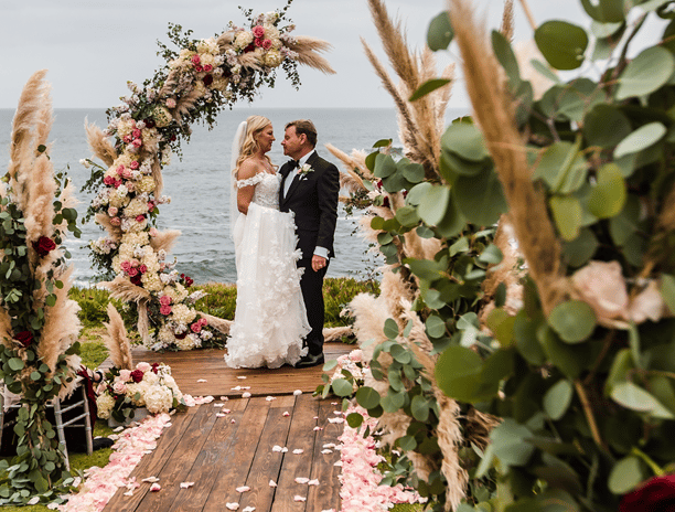 bride and groom standing on woodend deck surrounded by flowers at cuvier park, la jolla