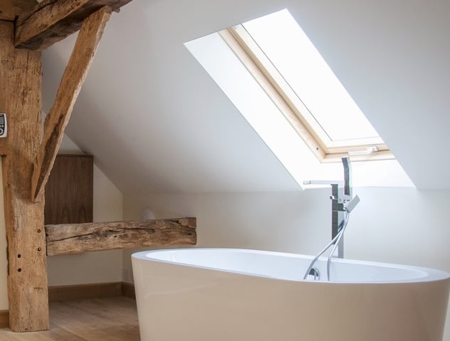 A modern rolltop bathtub deisgned around beams in a traditional barn home