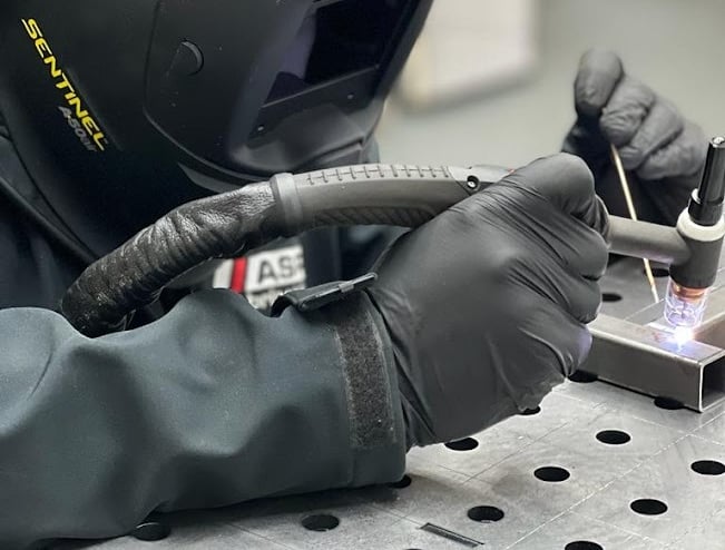 a person in a helmet and gloves is welding a piece of aluminium