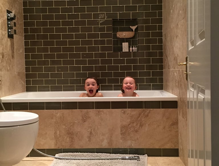 Two children pulling cheeky faces in the bath. 