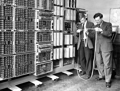 two men in suits and ties standing in front of a wall of many different types