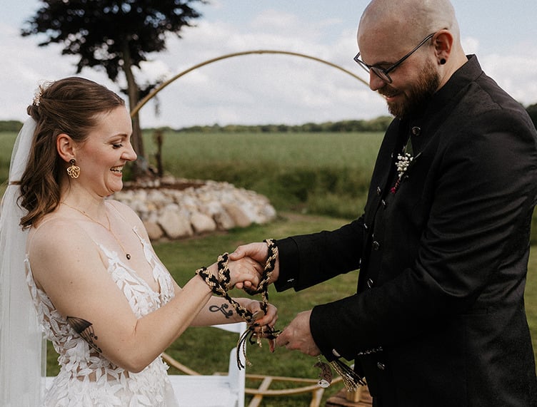 Knoten Ritual! das Hochzeitspaar bindet ein gold und schwarz geflechtetes Band um die eigenen Hände