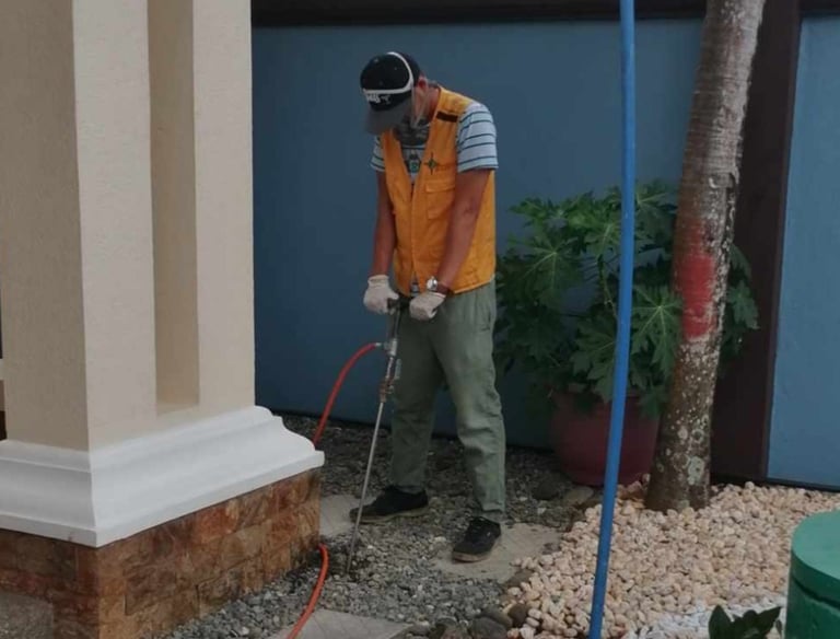 Professional pest control technician performing termite soil treatment at a residential building foundation.
