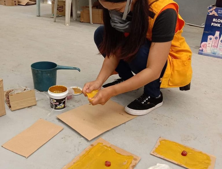 A worker in a safety vest and respirator mask applying industrial glue to cardboard sheets in a warehouse.