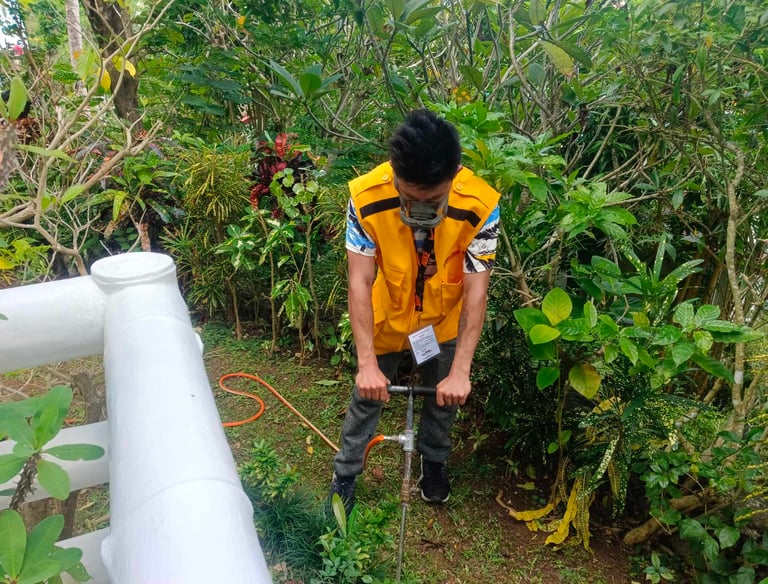 A pest control professional in a yellow vest performs soil treatment for termites in a garden.