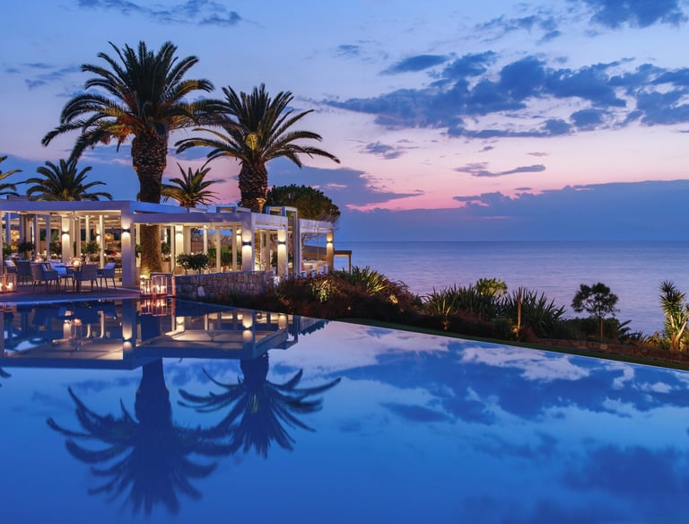 Luxury infinity pool reflecting palm trees and a sunset sky at Sani resort restaurant.