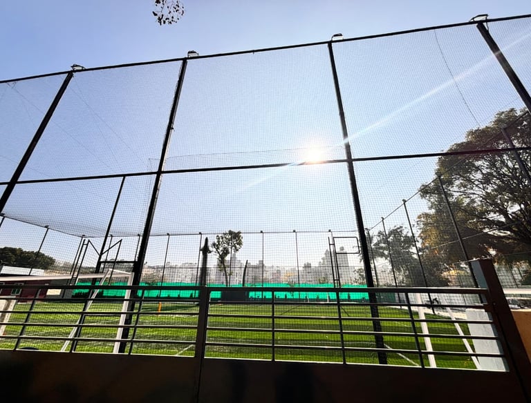 Technician fitting a sturdy sports net on a cricket practice cage under bright daylight.