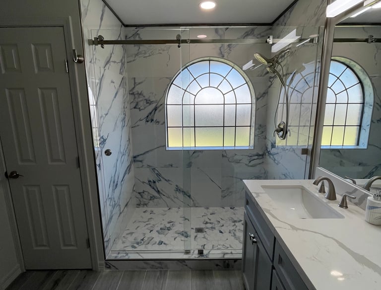 Modern master bathroom remodel featuring a walk-in marble shower with glass doors and arched window.