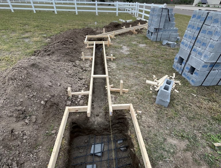 Concrete foundation forms and rebar prepared for a residential fence installation with cinder blocks.