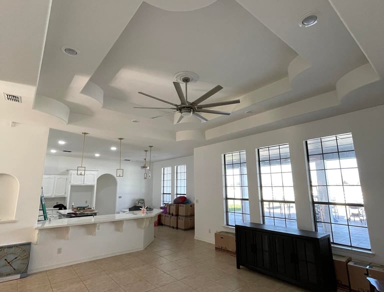 Spacious open concept living room with ornate tray ceiling, modern ceiling fan, and large windows.