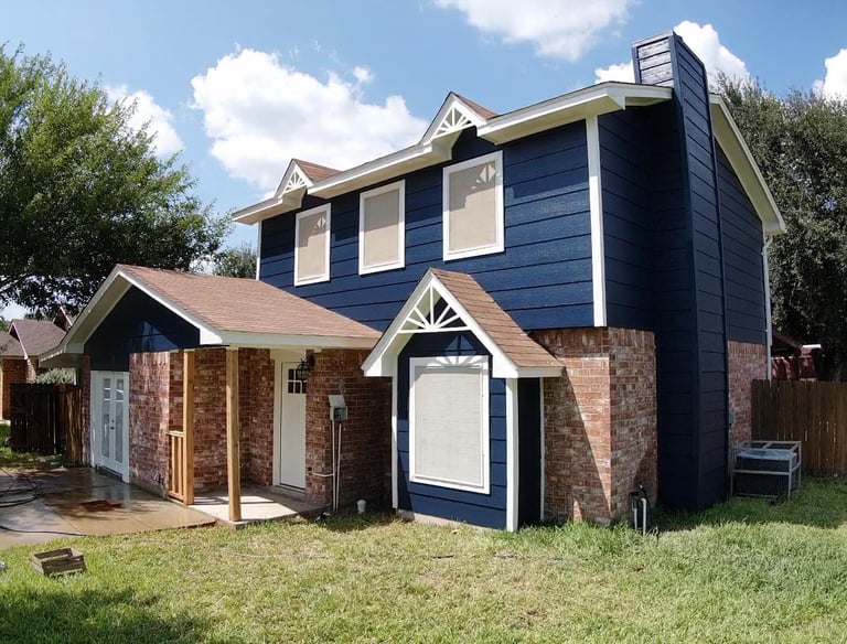 Two-story home with navy blue siding, red brick accents, and a brown shingle roof under a blue sky.
