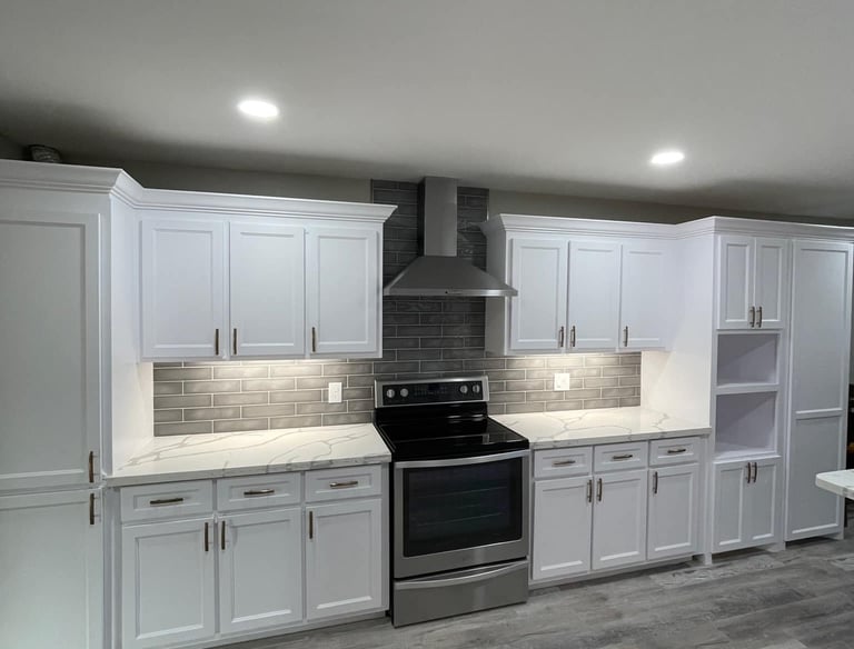 Modern white kitchen cabinets with marble countertops, grey subway tile backsplash, and stainless steel appliances.