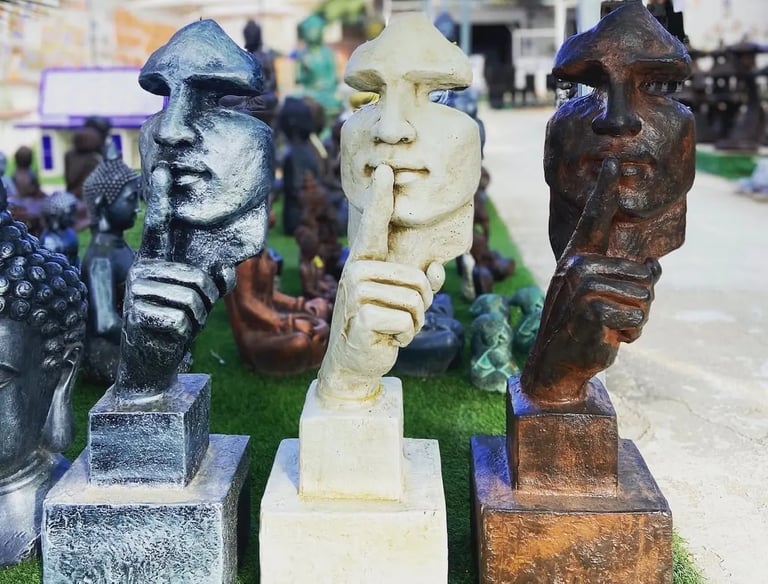Three silence statues in silver, white, and bronze finishes holding a finger to their lips.