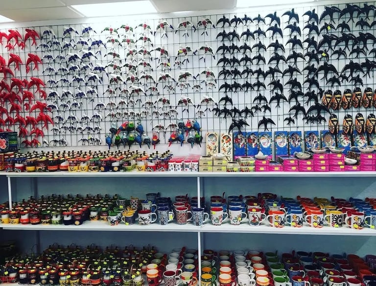 A colorful souvenir shop display featuring ceramic bird figurines and patterned coffee mugs on shelves.