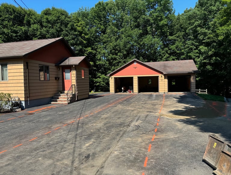 Residential asphalt driveway with orange marking lines leading to a three-car detached garage.