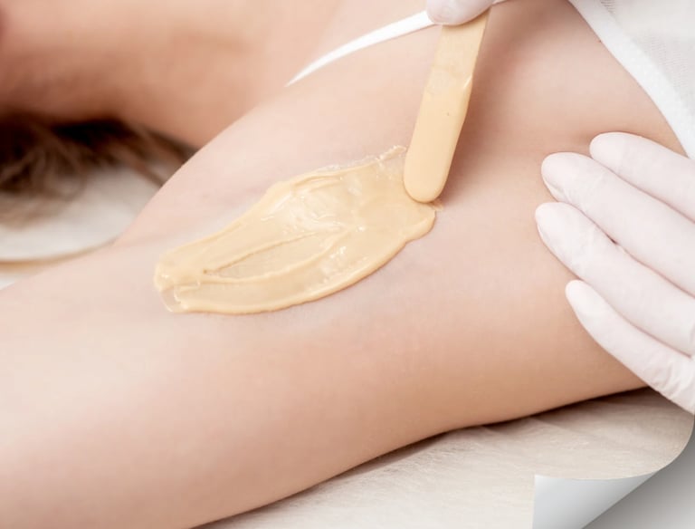 Professional esthetician applying warm sugar wax to a woman's underarm for hair removal.
