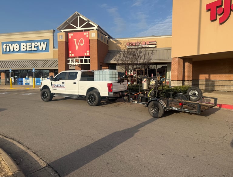 White service truck with trailer parked outside retail stores for commercial property maintenance.